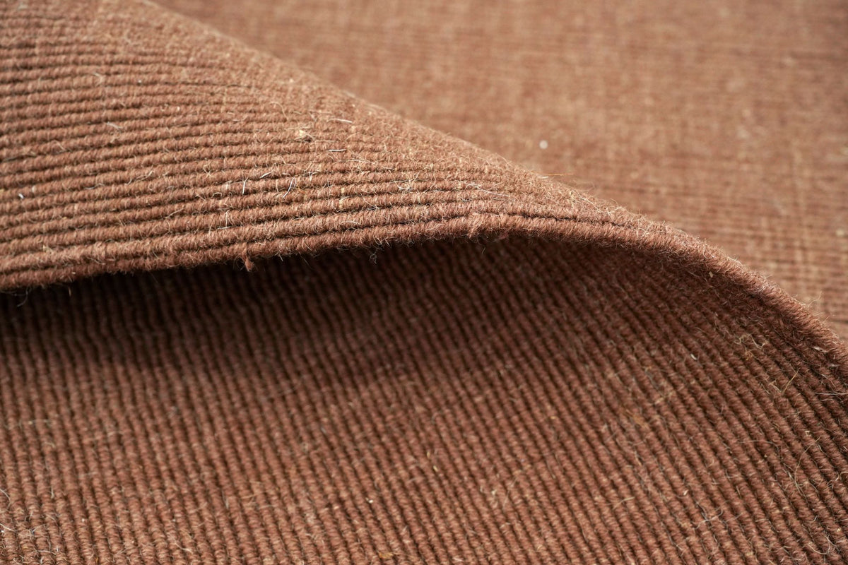 Cabra Wool & Jute Rug in Rust turned back in soft folds, a firm handloom weave of New Zealand wool and jute.