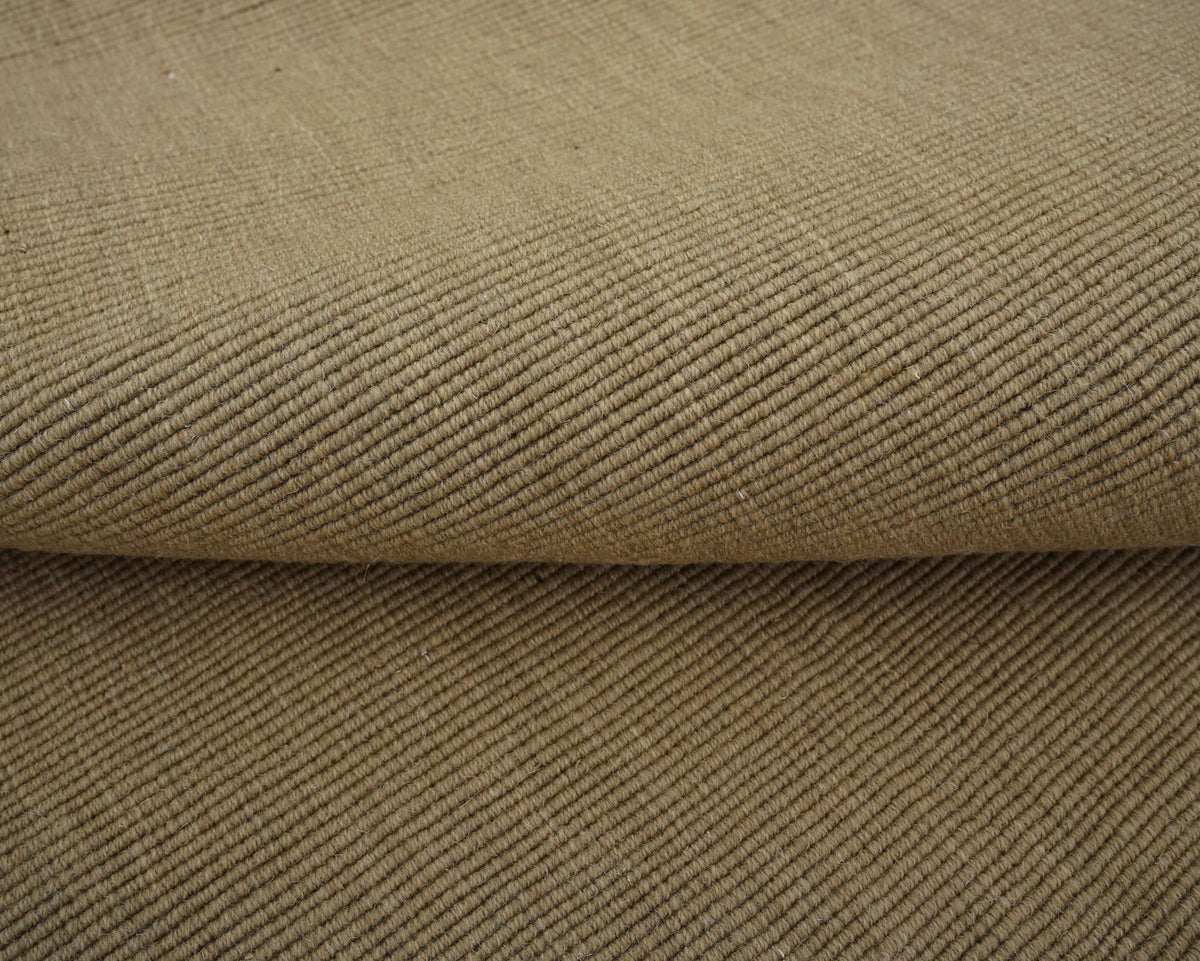 Cabra Wool & Jute Rug in Sand folded over itself, a light, flat handloom weave of New Zealand wool and jute.