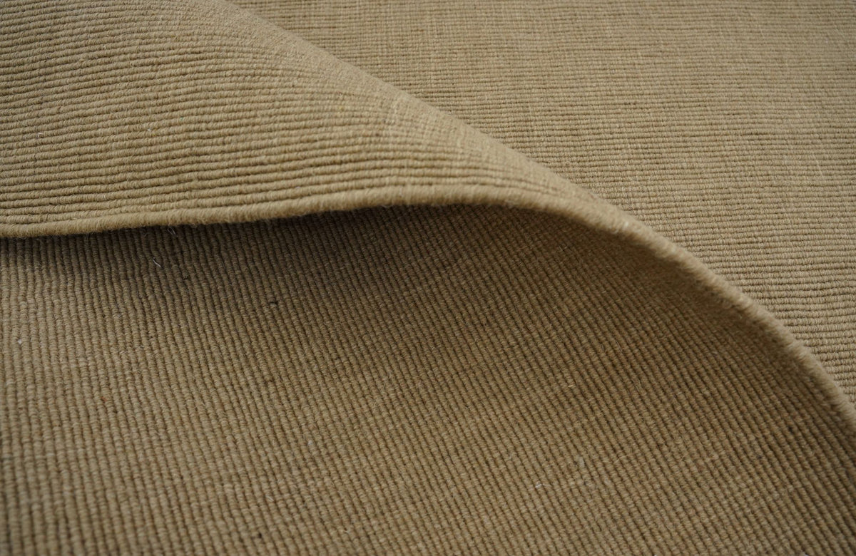 Cabra Wool & Jute Rug in Sand folded at the corner, a flat handloom weave of New Zealand wool and jute.