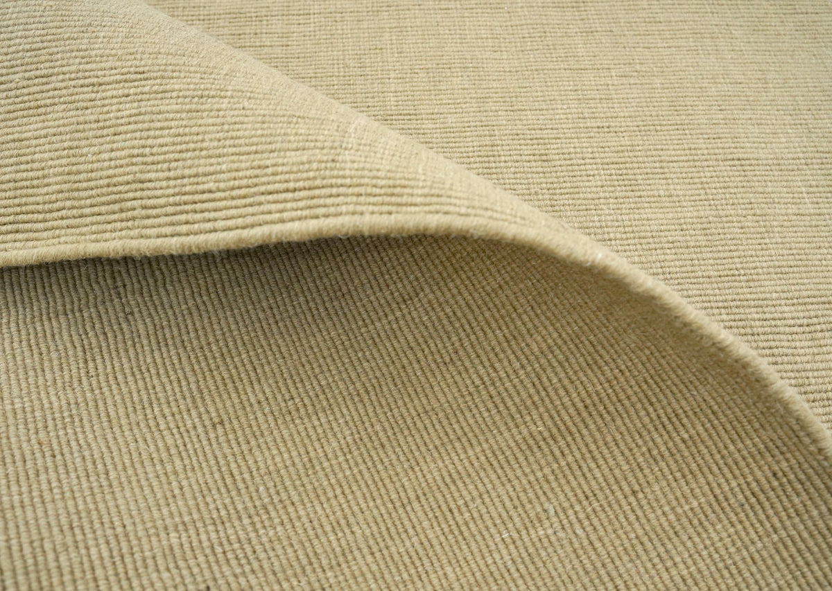 Cabra Wool & Jute Rug in Sand folded over itself, a firm handloom weave of New Zealand wool and jute.