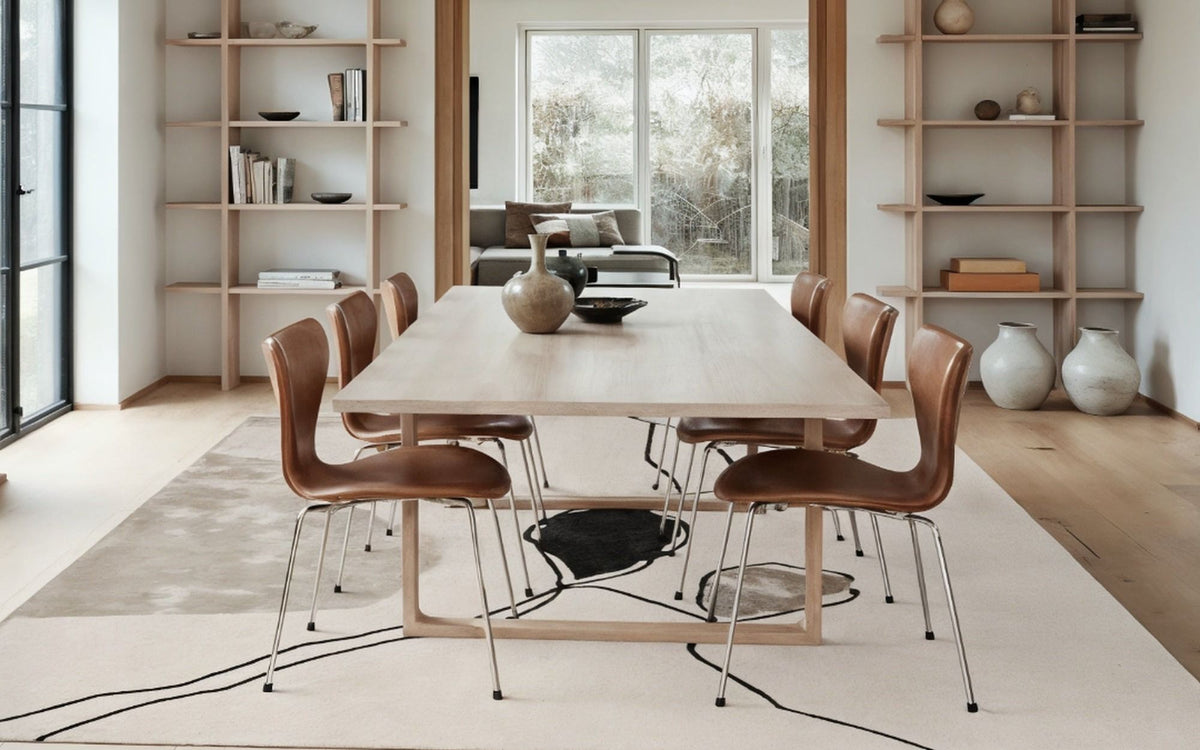 Concept Silk Rug in a dining room, a pale hand tufted Botanical Silk rug with fine dark lines under a long table.