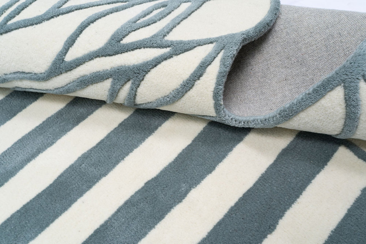 Euphoric Wool Rug folded back on itself, grey blue stripes and outlined leaf forms on ivory hand tufted New Zealand wool.