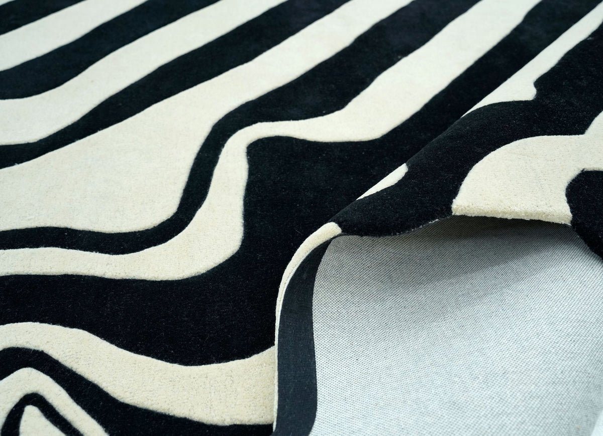 Fluid Wool Rug folded back at the edge, hand tufted New Zealand wool in black and ivory curves, showing the backing.