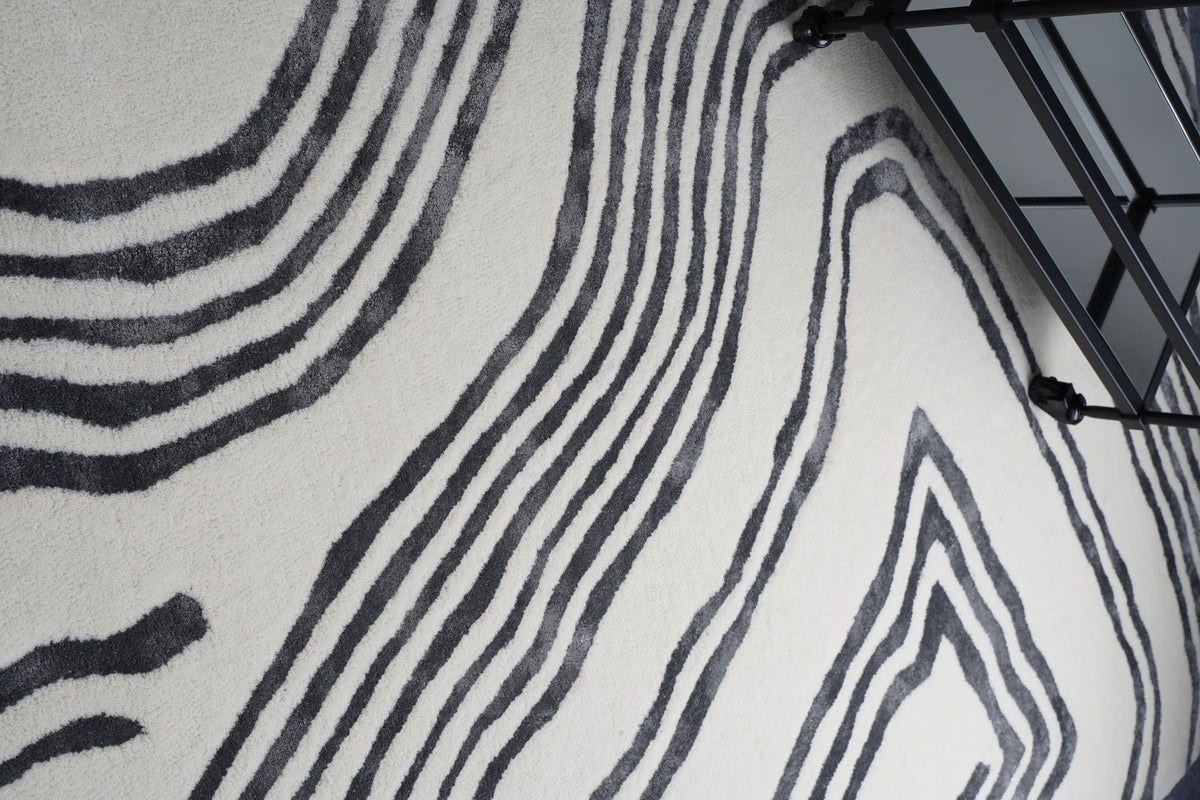 Livid Wool & Silk Rug seen from above beside a black metal side table, hand tufted New Zealand wool and Botanical Silk in flowing dark lines.