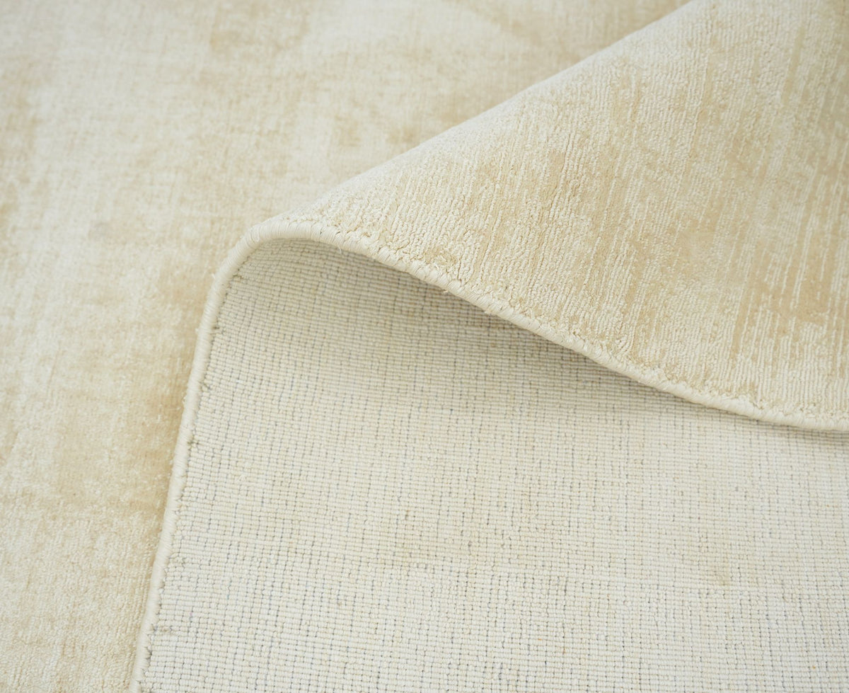 Nuva Silk Rug in Beige folded at the corner, handloom Botanical Silk with a soft sheen across the low pile.