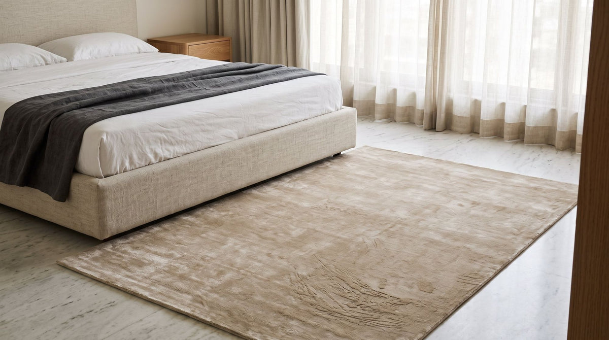 Luma Silk Rug beside a bed in a calm bedroom, handloom Botanical Silk on a pale stone floor.