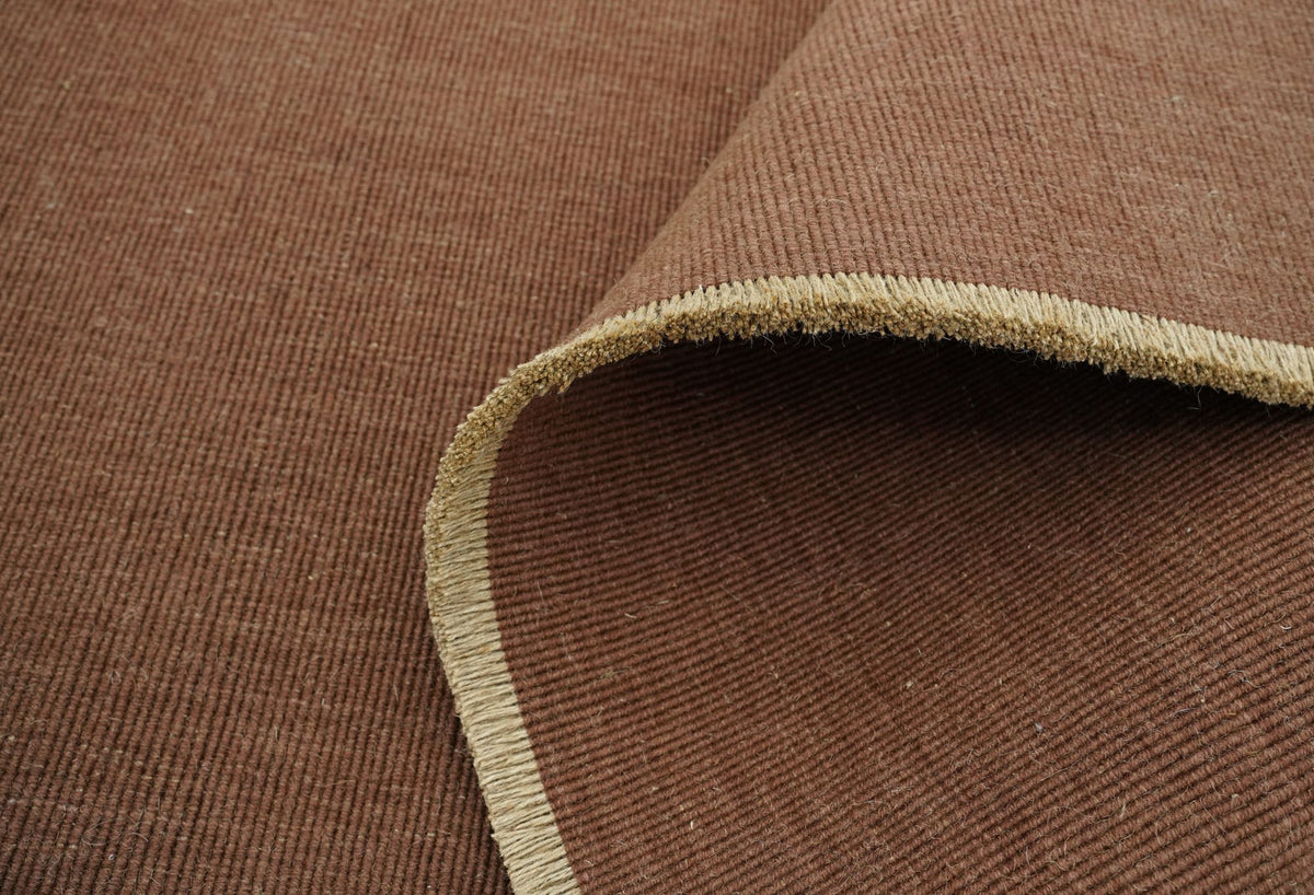 Cabra Wool & Jute Rug in Rust folded back at the corner, handloom New Zealand wool and jute with a pale bound edge.