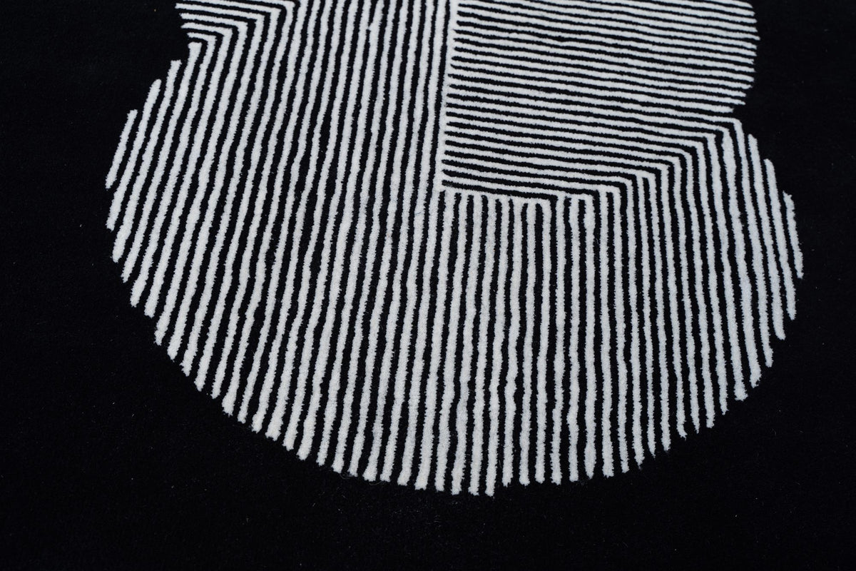 Clique Wool Rug in Pitch Black close up, hand tufted New Zealand wool with an ivory circular form of fine lines on a black field.