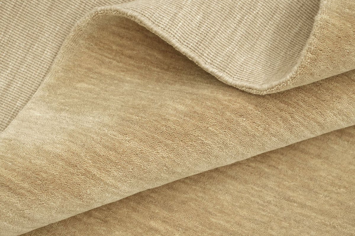 Grain Wool Rug in Sandstone folded at the corner, handloom New Zealand wool in a warm sandy tone with a close texture.