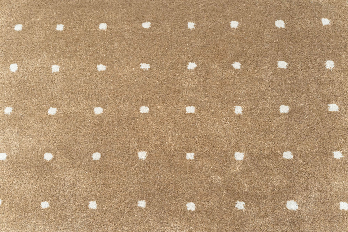 Hem Rug close up, hand tufted New Zealand wool with small ivory points on a warm camel field.