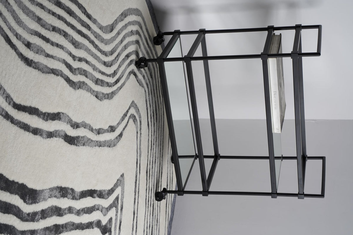Livid Wool & Silk Rug, ivory drawn with clouded charcoal lines, under a black steel and glass display stand.