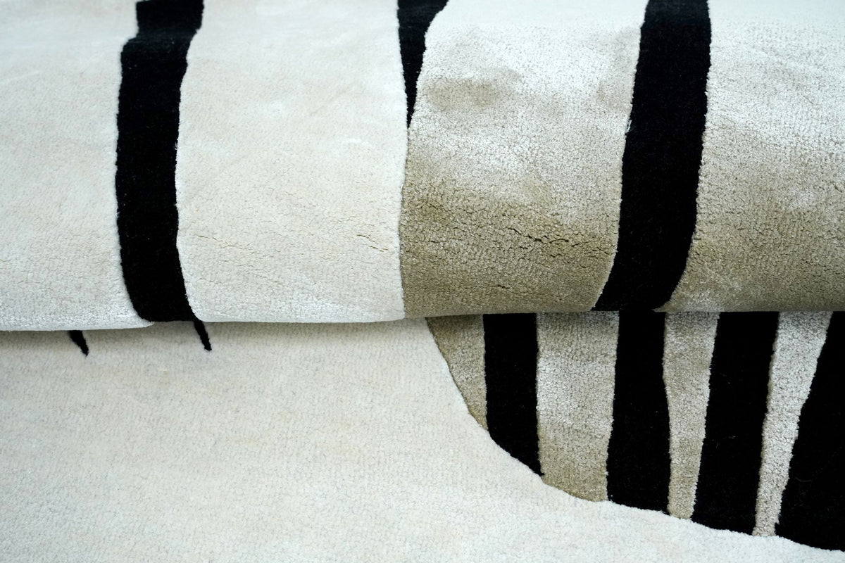 Lyra Wool & Silk Rug rolled at the edge, black lines over ivory New Zealand wool and pale Botanical Silk.