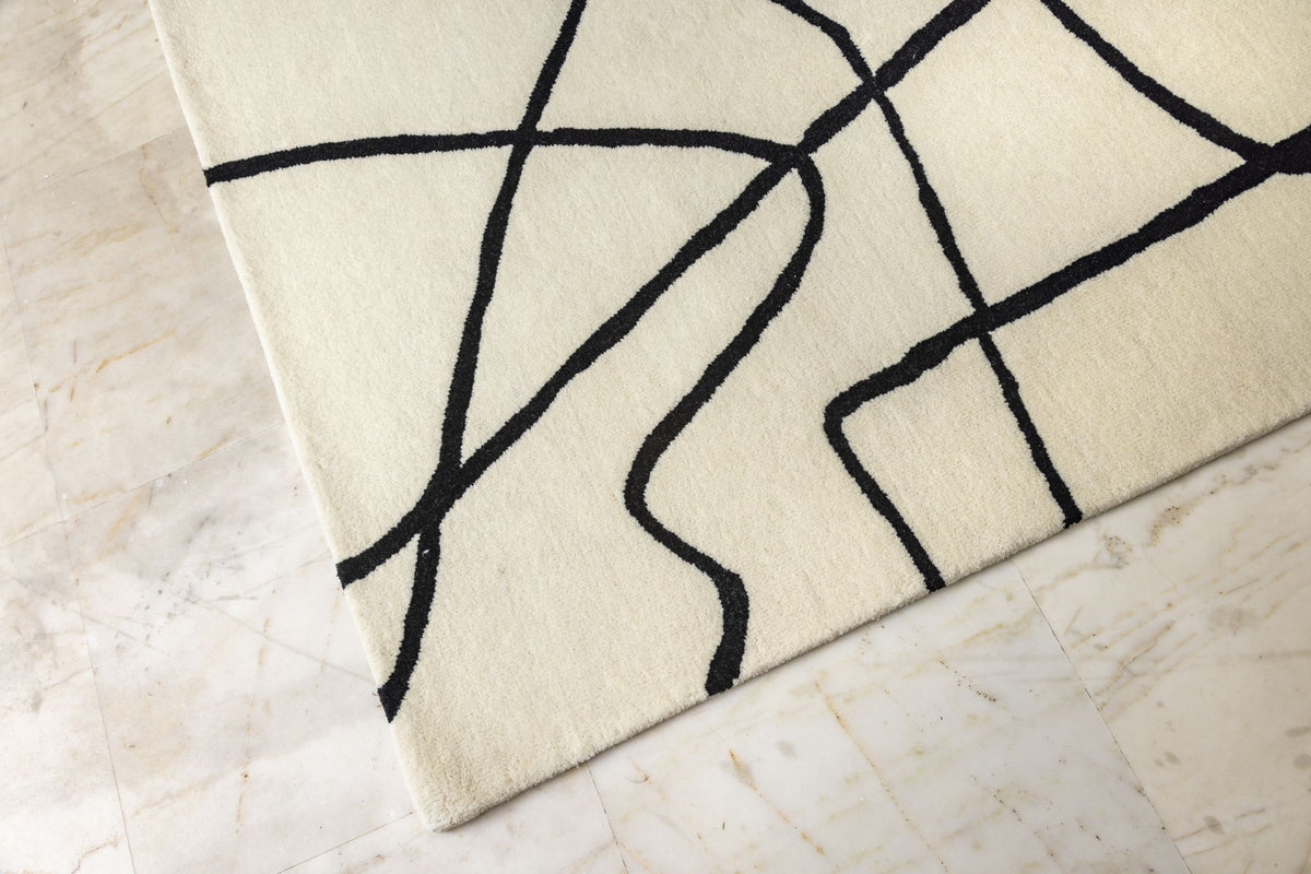 Tinker Wool Rug close up, hand tufted ivory New Zealand wool drawn with loose black lines, laid on a stone floor.