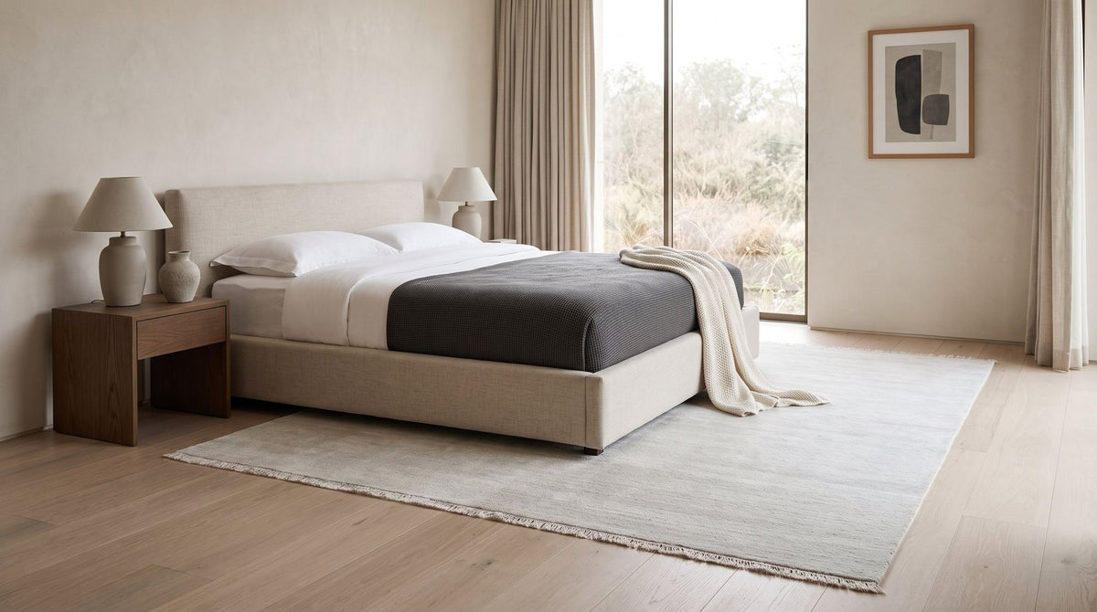 Cashmere Blend Rug in Salt under a bed in a styled bedroom, handloom wool and cashmere in the palest tone.