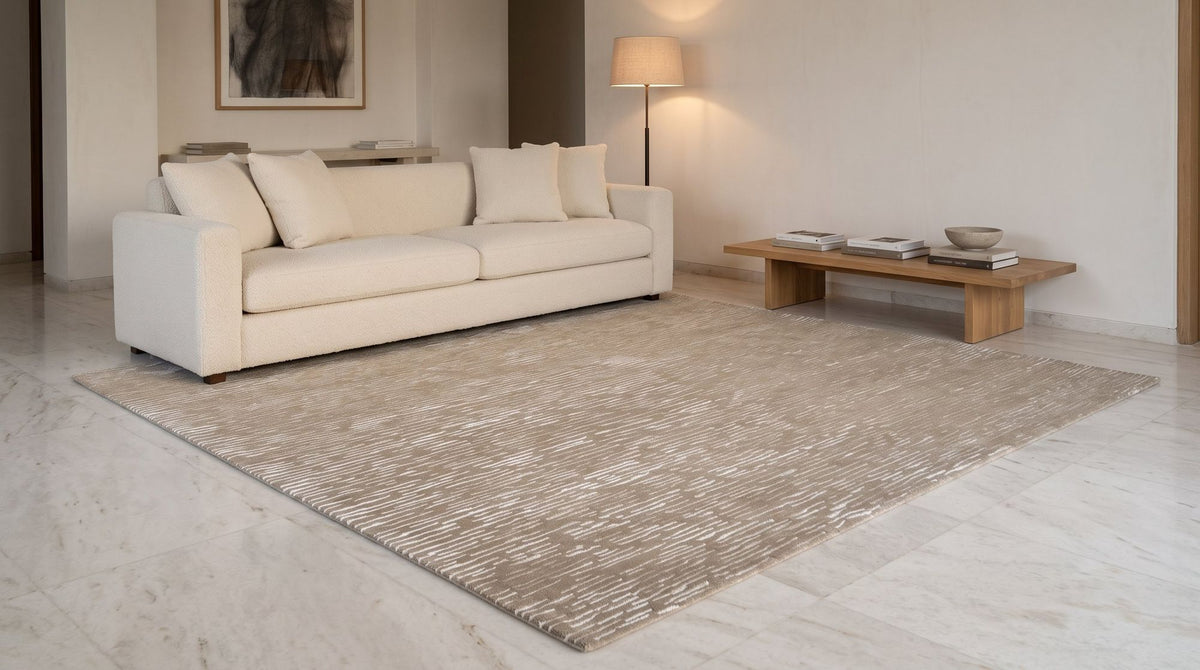 Cabella Wool & Silk Rug in Latte in a styled living room on a pale marble floor, shown as a styled render.