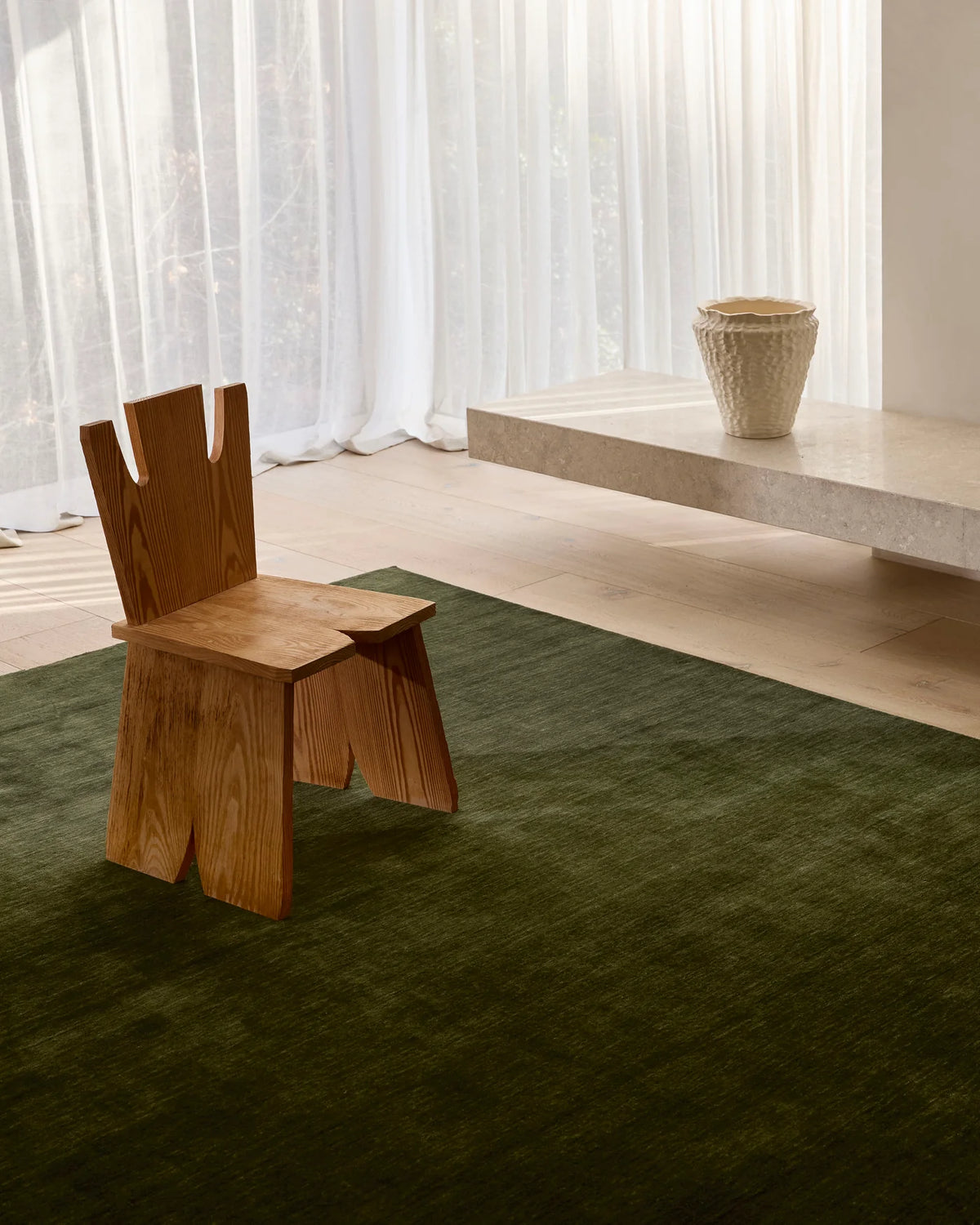 A deep green Rugberry rug with a sculptural wooden chair beside linen curtains